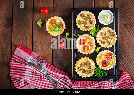 Pilze, Cheddar, Tomaten Törtchen auf Holz- Hintergrund. Mini Torten. Leckere Vorspeisen, Tapas, Snacks. Ansicht von oben. Flach Stockfoto