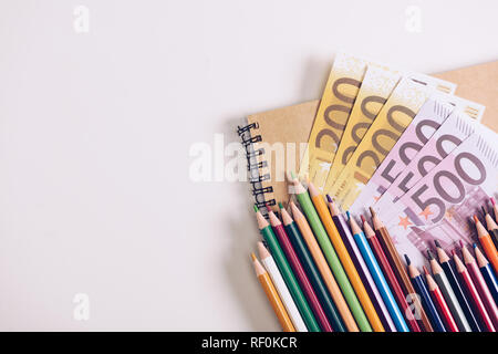 Set aus Holz Bunte Bleistifte auf Notebook in der Nähe von Euro Banknoten auf weißem Hintergrund Stockfoto