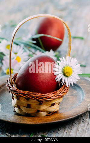 Hand gemalte rote Ostereier und daisy flower closeup in rustikalen Holzmöbeln Korb. Ostern Stillleben Feder Dekoration. Traditionelle handbemalte ester Eier Stockfoto