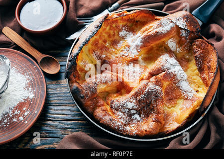 Niederländische baby Pfannkuchen bestreut mit Puderzucker In einer Pfanne mit himbeermarmelade und braunen Tuch auf einem alten rustikalen Tisch, klassisches Rezept, Ansicht von Abo Stockfoto