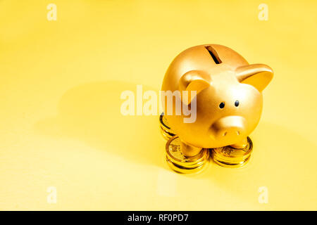 Sparschwein stehend auf den Stapel der goldenen Münze auf gelben Hintergrund. Das chinesische Neujahr. Jahr der Erde Schwein Stockfoto