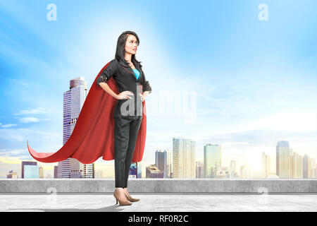 Junge asiatische Geschäft Frau mit rotem Umhang, der auf der Dachterrasse mit Stadtansichten Hintergrund Stockfoto