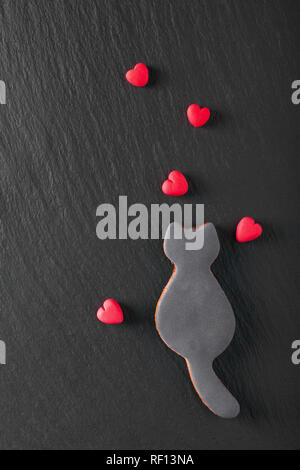 Valentine Hintergrund edibale genießbare Single black cat Cookies und Fondantzucker roten Herzen auf schwarzen Hintergrund mit Kopie Raum Stockfoto