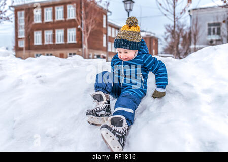 Eine heitere und fröhliche Junge im Alter von 3-5 Jahre, slithers aus einer schneeverwehung auf einem Canyon, spielt in einem Schnee-bedeckten Stadt im Winter. Spielen im Winter auf der Eisbahn. Stockfoto