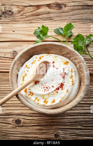 Schüssel aus erfahrenen erfrischende Indischen raita mit natürlichen griechischer Joghurt und gekrönt mit Gewürzen in einem rustikalen Holzmöbeln Schüssel auf Holz Hintergrund in einer Ansicht fr Stockfoto