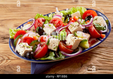 Schüssel, gesunde, frische Griechischer Salat mit Feta Käse, Oliven, Gurken, Salat, Zwiebeln und Tomaten gewürzt mit Kräutern auf einem Holztisch Stockfoto