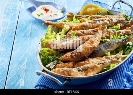 Gesunde, mediterrane oder griechische Vorspeise von gebratene Sardinen in Teig auf einem Bett von frischem Salat serviert in einem vintage Schüssel über einem blauen Holz Hintergrund wi Stockfoto