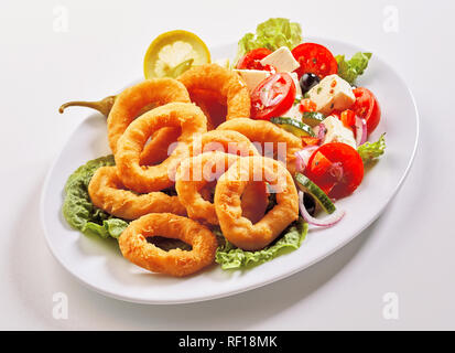 Lecker Mittagessen mit Meeresfrüchten mit zerschlagenen Frittierte Tintenfischringe und Griechischer Salat mit Feta und Oliven auf einem ovalen Teller serviert auf Weiß Stockfoto