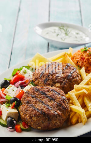 Würzige gegrillte Griechische bifteki Fleisch Kugeln mit einem frischen Salat mit Feta und Oliven serviert, Pommes frites und Tomate Reis Stockfoto