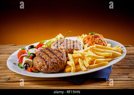 Bifteki, oder würzigen Fleischbällchen von Hackfleisch, Lamm- und Rindfleisch und frische Griechischer Salat mit Feta und Oliven mit Tomate Reis Pilav und Pommes frites serviert. Stockfoto