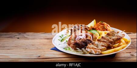 Banner mit einem traditionellen griechischen Grillteller Teller mit Tomaten Reis, Pommes und erfrischenden raiti Joghurt auf einem rustikalen Tisch mit kopieren Stockfoto