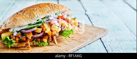 Griechische gyros Burger mit gerösteten Scheiben kebab Fleisch, Pommes frites und Salat Beilagen auf einem crusty Roll auf einem Holzbrett serviert, panorama Banner mit Co Stockfoto