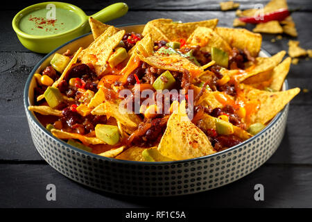 Würzige mexikanische Chili con carne gratiniert mit Nachos und gewürfelte Avocado pear gekrönt und mit Guacamole serviert. Stockfoto