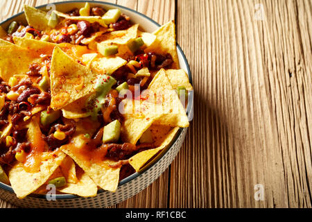 Hot Spicy Chili con carne mit Nachos recipe gekrönt mit geschmolzenem Käse, frisch gewürfelte Avocado und Koriander serviert in einem flachen Teller hohen Winkel auf Tropfen, Stockfoto