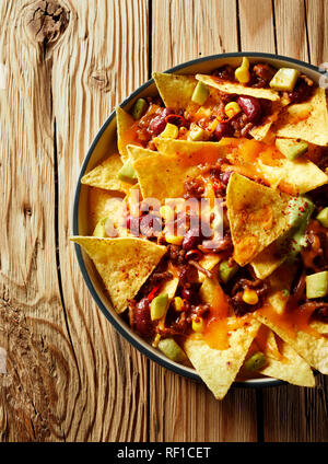 Würzige mexikanische Chili con carne mit Nachos überbacken und frischen avocado Birne in eine Ofenform auf rustikalen Holzmöbeln serviert in einer Ansicht von oben Stockfoto