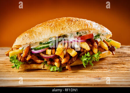 Griechische gyros Burger mit gerösteten geschnittenes Fleisch, Salat, Zwiebeln, Gurken, Tomaten und Pommes frites auf einem frischen Brötchen auf rustikalem Holz Stockfoto