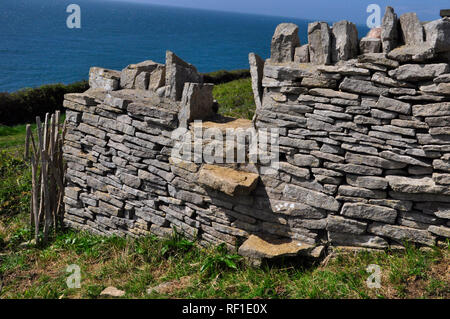 Trockenmauer mit Stil in gebaut auf der Isle of Purbeck, Dorset. Grobe Kalkstein Mauer teilt abfallenden Küsten Felder mit dem Meer im Hintergrund. Stockfoto