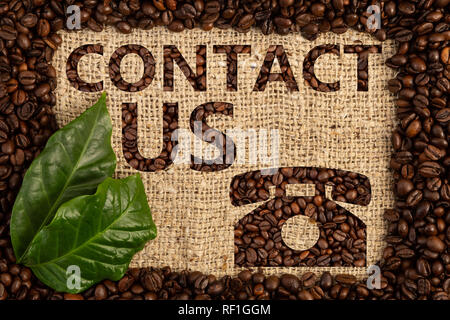 Kontakt Konzept mit Phone Symbol mit Kaffeebohnen auf Braun sackleinen Hintergrund mit grünen Blättern geschrieben Stockfoto