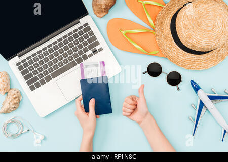 7/8-Ansicht von Frau mit Pässe und Flugtickets dabei Daumen oben-Geste in der Nähe von Laptop, Ohrhörer, Sonnenbrille, Muscheln, Flip Flops, Spielzeug pl Stockfoto