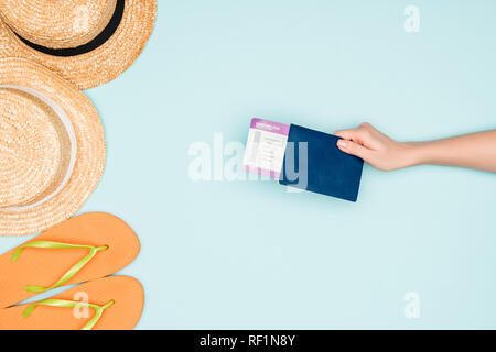 7/8-Ansicht von Frau mit Flugticket und Pass in der Nähe von Flip Flops und Strohhüte auf blauem Hintergrund Stockfoto