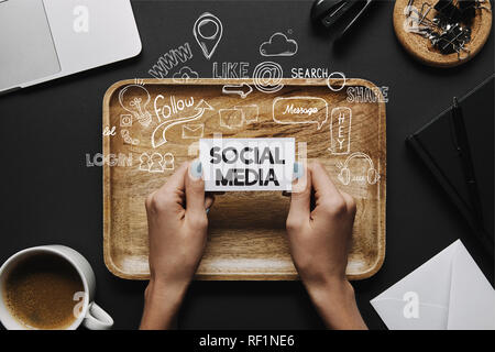 Weibliche Hände holding Business Card mit 'Social Media'-Schriftzug und Icons, die auf schwarzen Hintergrund mit Fach und Briefpapier Stockfoto