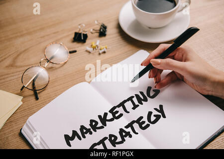 Teilweise mit Blick auf die Frau schreiben Marketing Strategie im Notebook am Arbeitsplatz mit Brillen und Tasse Kaffee Stockfoto