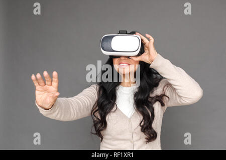 Freestyle. Reife Lady in der Virtual reality Headset stehen isoliert auf grau Video berühren Raum glücklich Stockfoto