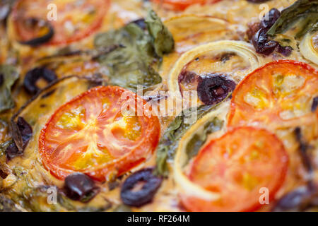 Quiche ist eine Eierspeise mit Zutaten wie Tomaten, Spinat, Zwiebeln und Oliven. Stockfoto