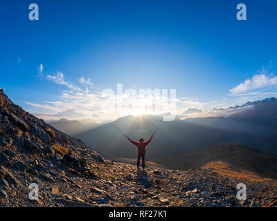 Grenzregion Italien Schweiz, jubelnde älterer Mann mit Wanderstöcken in Berglandschaft am Piz Umbrail-pass Stockfoto