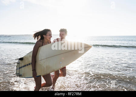 Frankreich, Bretagne, glückliches junges Paar mit Surfbrett im Meer läuft Stockfoto