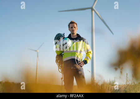 Techniker stehen ein Feld an einem Windpark mit Kletterausrüstung Stockfoto