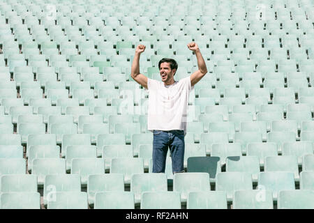 Ein junger stattlicher Mann steht in einem leeren Stadion allein und feiert einen Sieg und zeigt ein Gefühl des Erfolgs Stockfoto