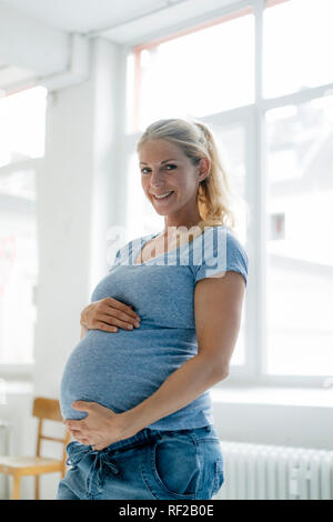 Portrait von lächelnden schwangere Frau steht am Fenster Stockfoto