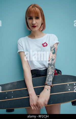 Portrait von Cool junge Frau mit Carver skateboard stehend an türkisblauen Wand Stockfoto