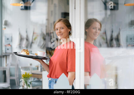 Portrait von lächelnden jungen Frau mit Kaffee und Kuchen in einem Cafe Stockfoto