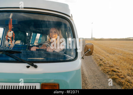 Glückliche junge Frau, die mit ihrem Wohnmobil ganz in ländlichen Landschaft