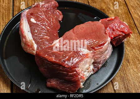 Zwei große Frische und saftige Fleisch Steaks liegen in einer schwarzen Platte auf einem hölzernen Hintergrund. Stockfoto