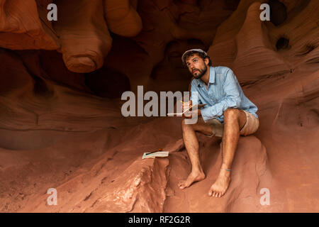 Junger Mann in einer Höhle sitzen, Notizen Stockfoto