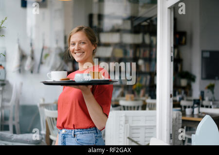 Portrait von lächelnden jungen Frau mit Kaffee und Kuchen in einem Cafe Stockfoto