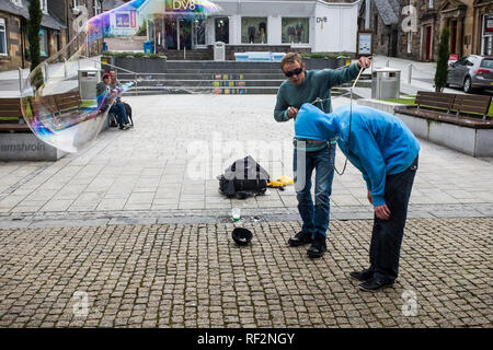 Jugend in Blau hoody Freiwillige für Street Performer mit großen Blasen zeigen, Fort William Stadtzentrum highlands Schottland Großbritannien Stockfoto