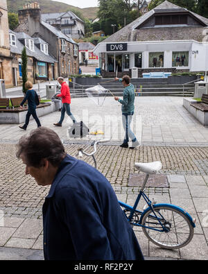 Alte Frau und paar Spaziergang, vorbei an einem geparkten blauen Fahrrad und Street Performer in Fort William High Street highlands Schottland Großbritannien Stockfoto