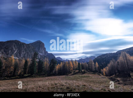 Berge schöne Nacht im Herbst in den Dolomiten, Italien. Landschaft mit Bäumen im alpinen Tal, Wiese, Himmel mit Wolken, Mond, Sterne. Stockfoto