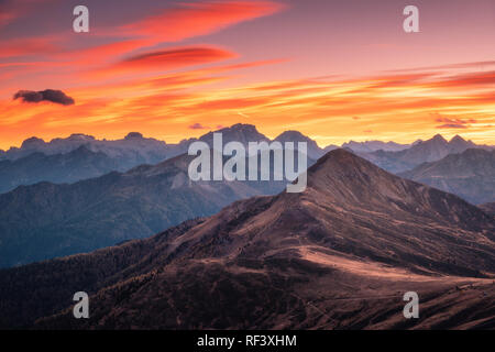 Berge bei Sonnenuntergang im Herbst in den Dolomiten, Italien. Landschaft mit Felsen, Wald auf Hügeln und orange sky mit roten Wolken am Abend. Autu Stockfoto
