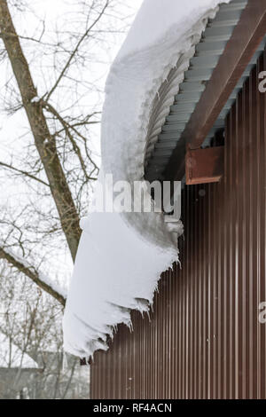 Snowdrift vom Dach herunterhängen. Dach mit Schnee und Eiszapfen Gesims Stockfoto