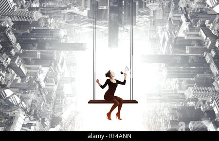 Frau mime im schwarzen Anzug sitzt auf Swing. Mixed Media Stockfoto