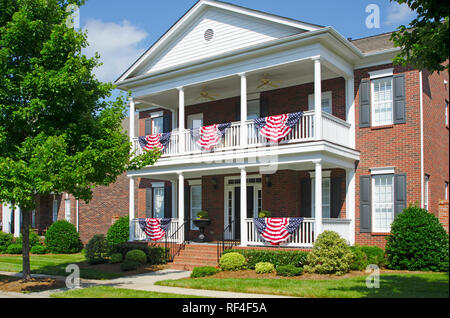 Patriotische amerikanische Flagge Bunting hing an einem Backstein Haus mit einem weißen Veranda Stockfoto