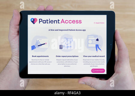 Ein Mann sieht der Patient Access Website auf seinem iPad tablet device, Schuß gegen einen hölzernen Tisch top Hintergrund (nur redaktionelle Nutzung). Stockfoto