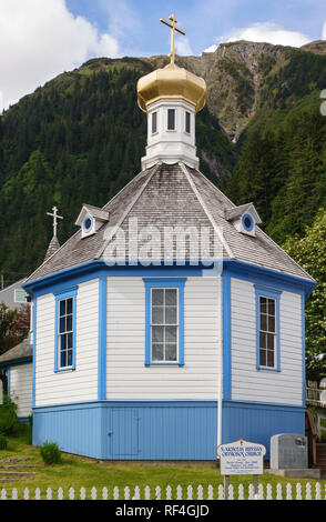 Steile Berghänge bieten eine dramatische Kulisse für St. Nikolaus bei der Russischen Orthodoxen Kirche, Juneau, Alaska. Dieses historische Wahrzeichen hat einen Zwiebelturm. Stockfoto