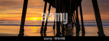 Die untergehende Sonne am Pier in Imperial Beach, Kalifornien mit den Silhouetten der Surfer warten auf Wellen. Stockfoto