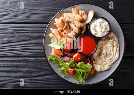 Mediterran Chicken Shawarma Schüssel mit Hummus, Gemüse, Salat und Sauce close-up auf einem Holztisch. horizontal oben Ansicht von oben Stockfoto